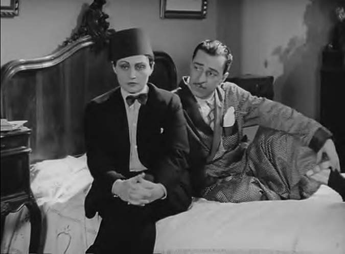 Ḥikmat (Assia Dagher), disguised as a man, sits on a bed beside her love interest, Tawfiq (Aḥmad Galal). Screenshot from Bint el-Basha el-Mudir (Daughter of the Pasha in Charge, 1938).